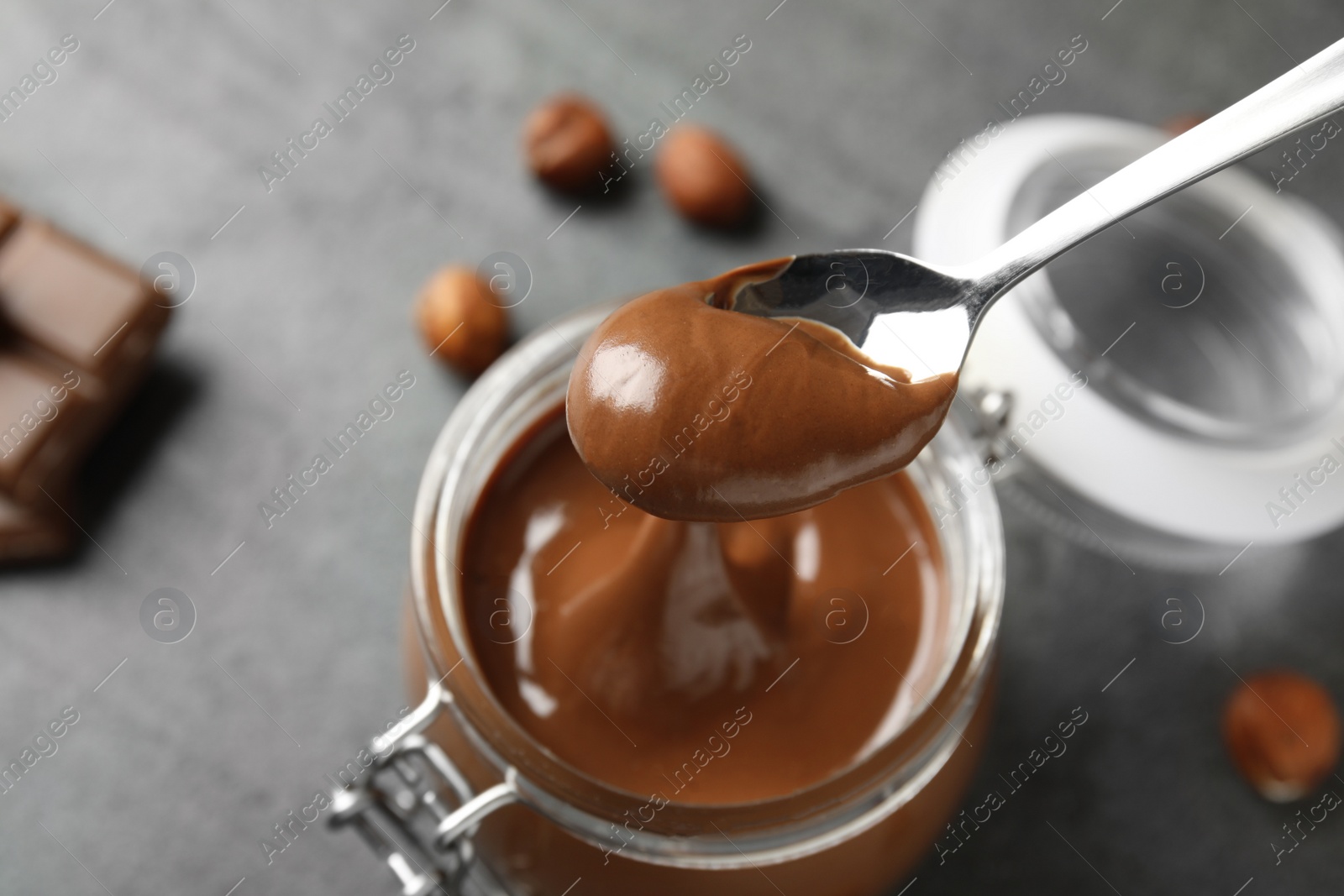 Photo of Spoon with tasty chocolate cream over full jar on table, view from above