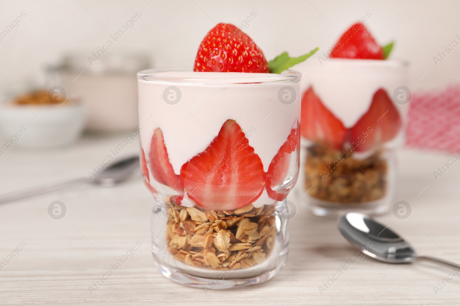 Photo of Glasses of tasty yogurt with muesli and strawberries served on white wooden table