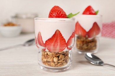 Photo of Glassestasty yogurt with muesli and strawberries served on white wooden table