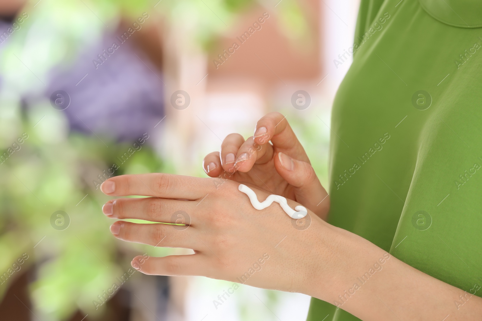 Photo of Young woman applying cream on her hands indoors, closeup