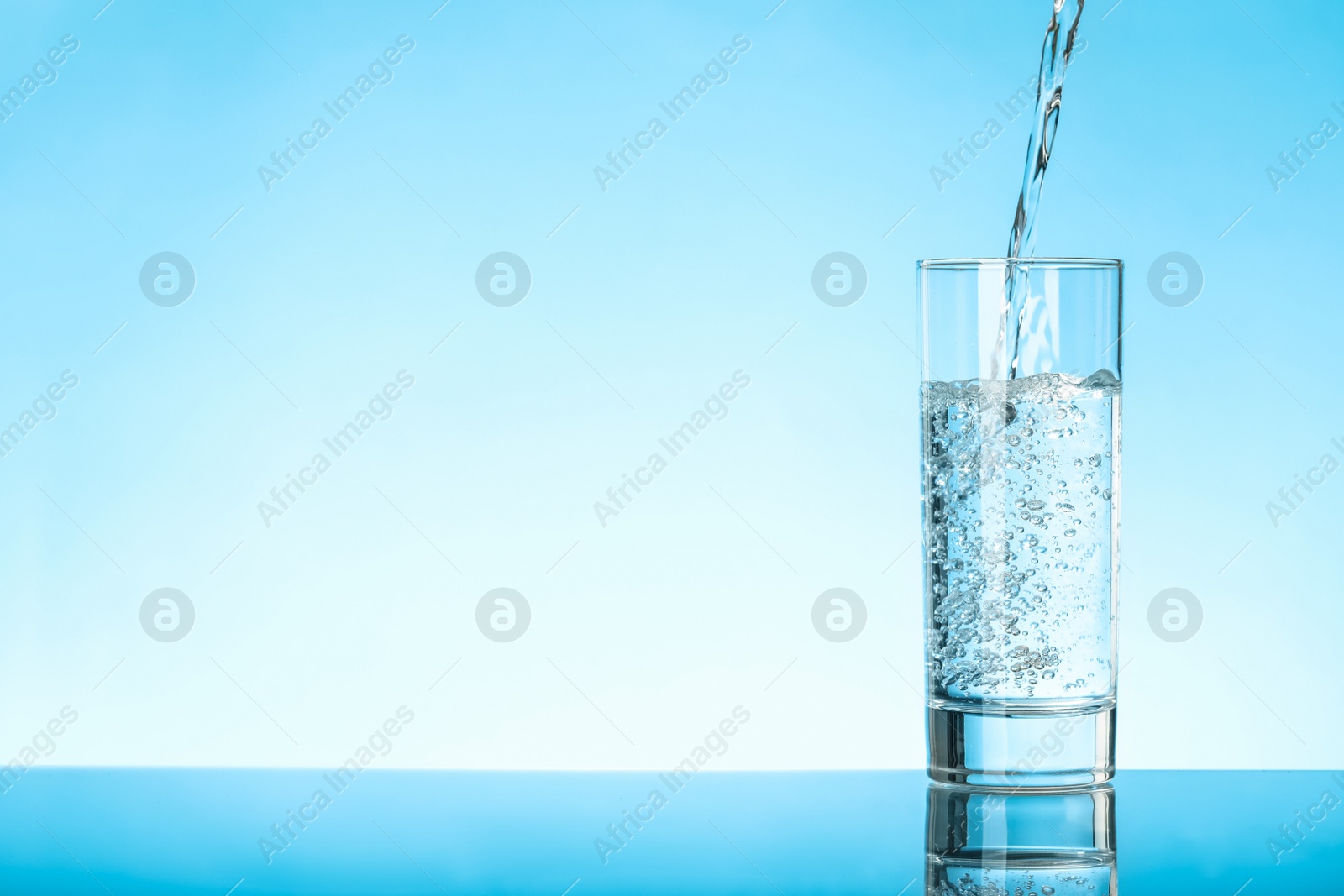 Photo of Pouring water into glass on blue background, space for text. Refreshing drink