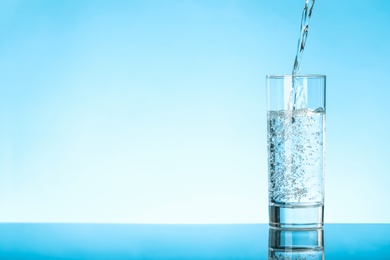 Pouring water into glass on blue background, space for text. Refreshing drink