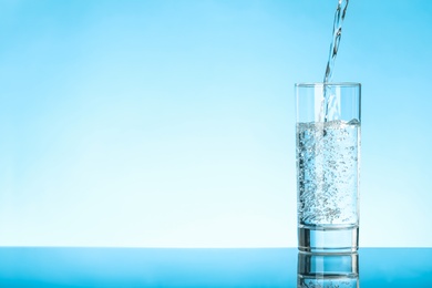 Photo of Pouring water into glass on blue background, space for text. Refreshing drink