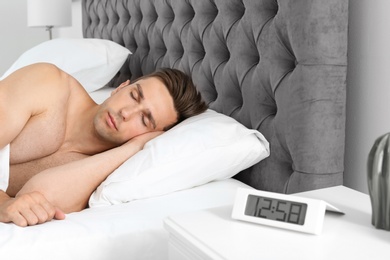 Young man sleeping in bed and alarm clock on nightstand at home