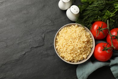 Photo of Delicious bulgur in bowl, dill, parsley and tomatoes on black table, top view. Space for text