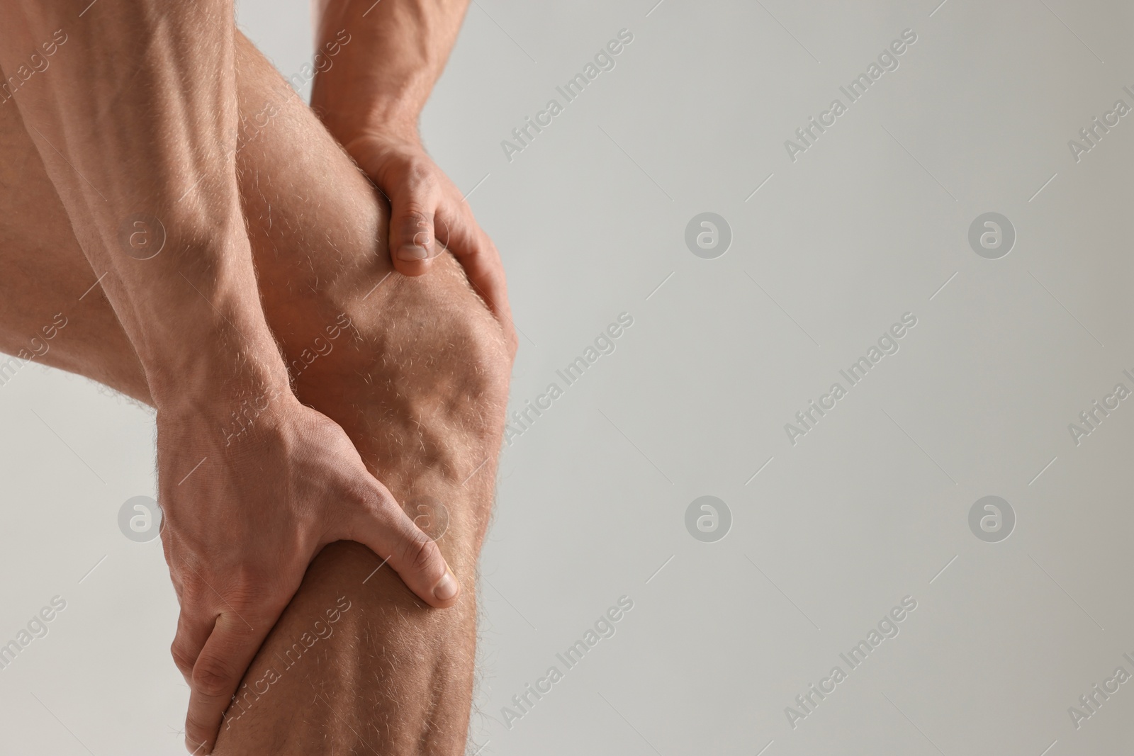 Photo of Man touching his muscular legs on light grey background, closeup. Space for text