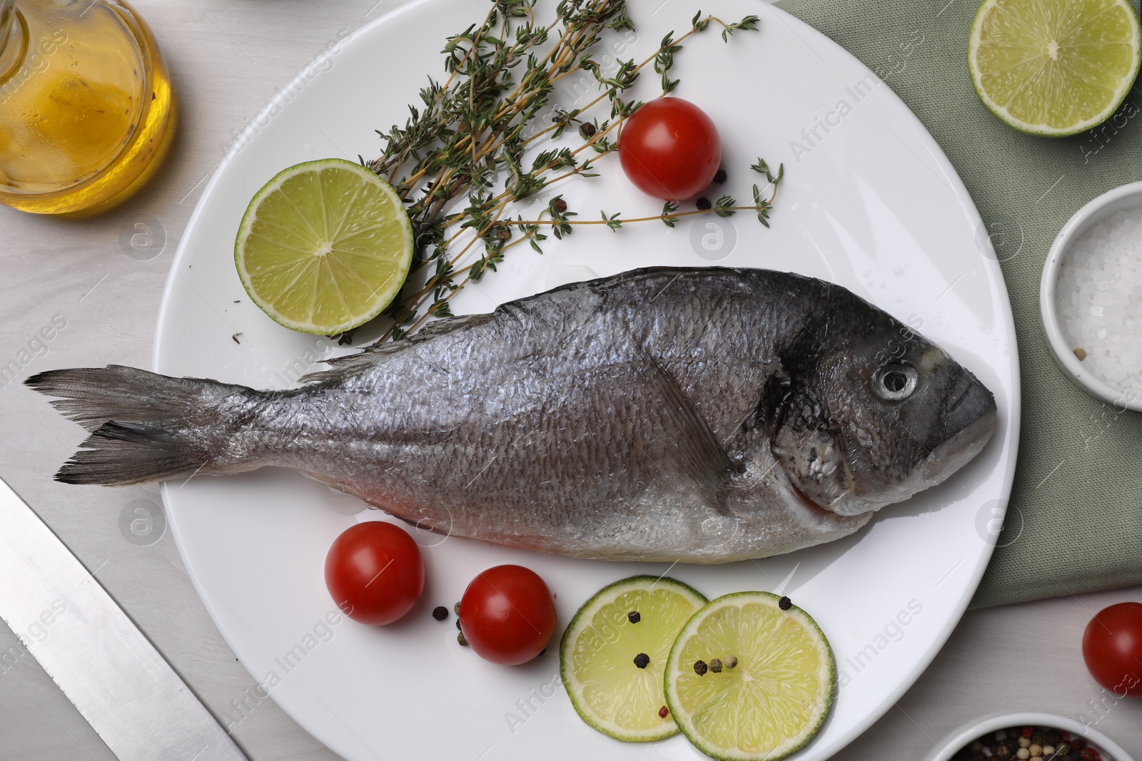 Photo of Raw dorado fish, lime, tomatoes and thyme on light table, flat lay