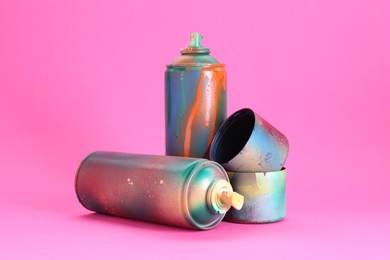 Photo of Spray paint cans with caps on pink background