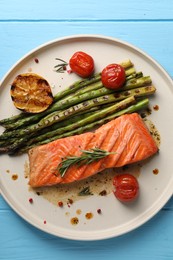 Photo of Tasty grilled salmon with tomatoes, asparagus and spices on light blue wooden table, top view
