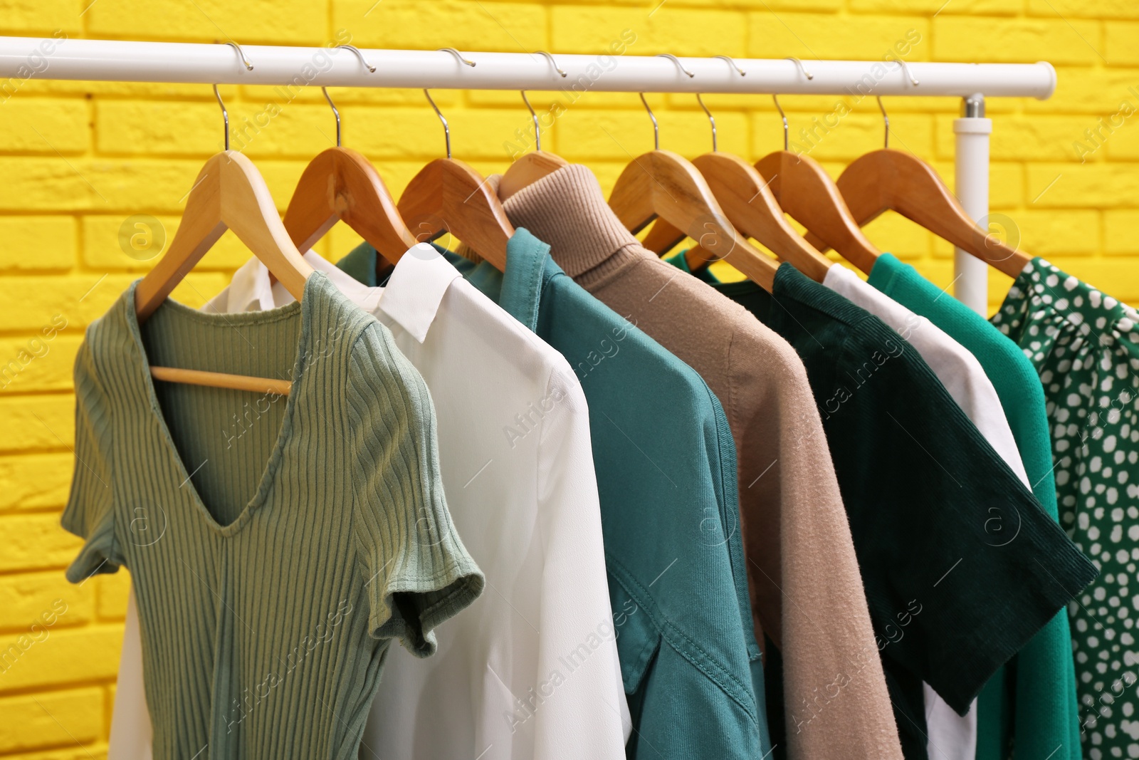 Photo of Rack with different stylish clothes near yellow brick wall