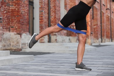 Photo of Woman doing exercise with fitness elastic band outdoors, closeup