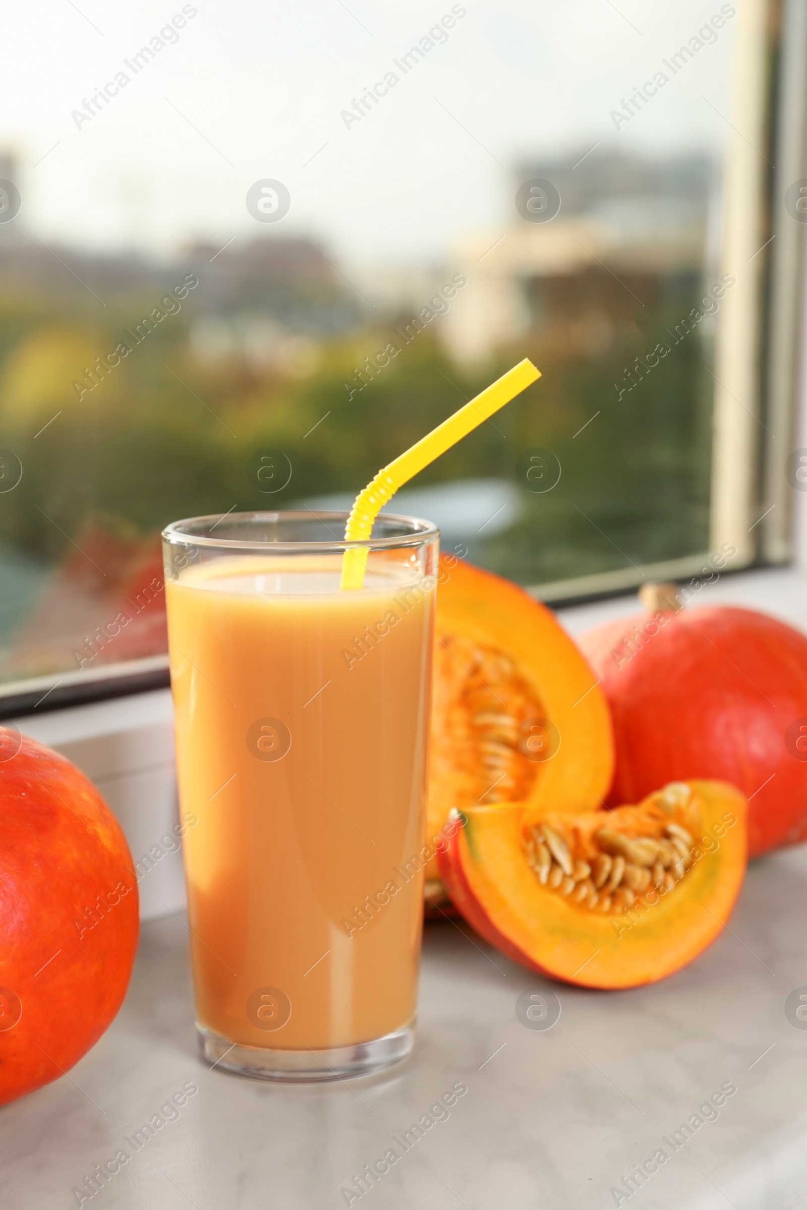 Photo of Tasty pumpkin juice in glass, whole and cut pumpkins on windowsill indoors