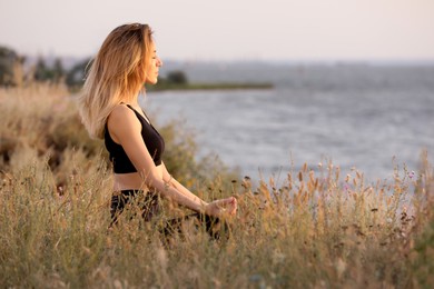Photo of Young woman meditating near river on sunny day, space for text