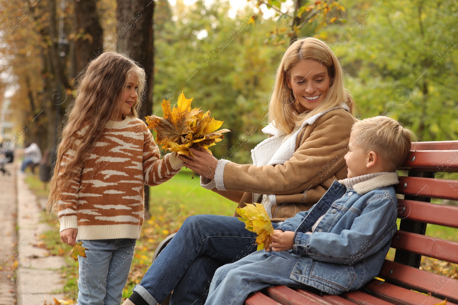 Photo of Happy mother and her children spending time together with dry leaves in autumn park