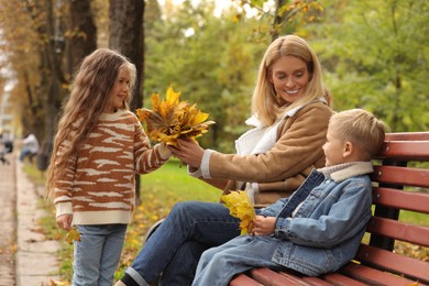 Happy mother and her children spending time together with dry leaves in autumn park