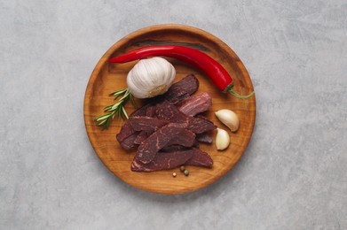 Plate with pieces of delicious beef jerky and spices on light grey table, top view