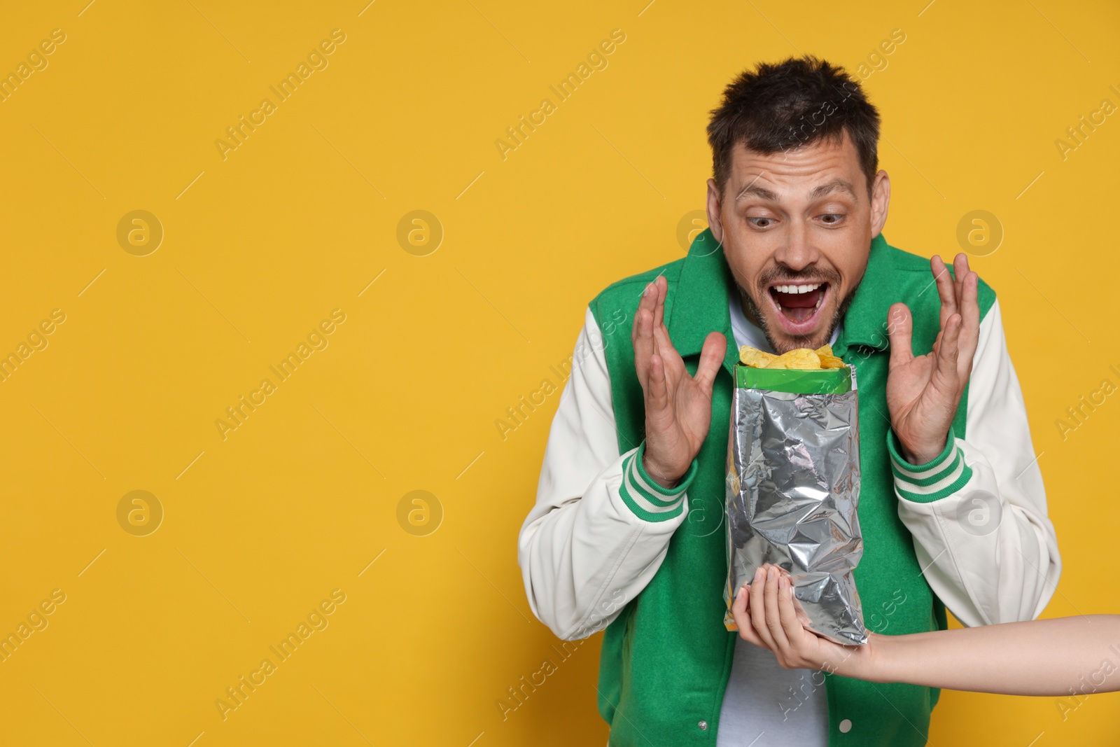 Photo of Woman offering tasty potato chips to excited man on orange background, space for text