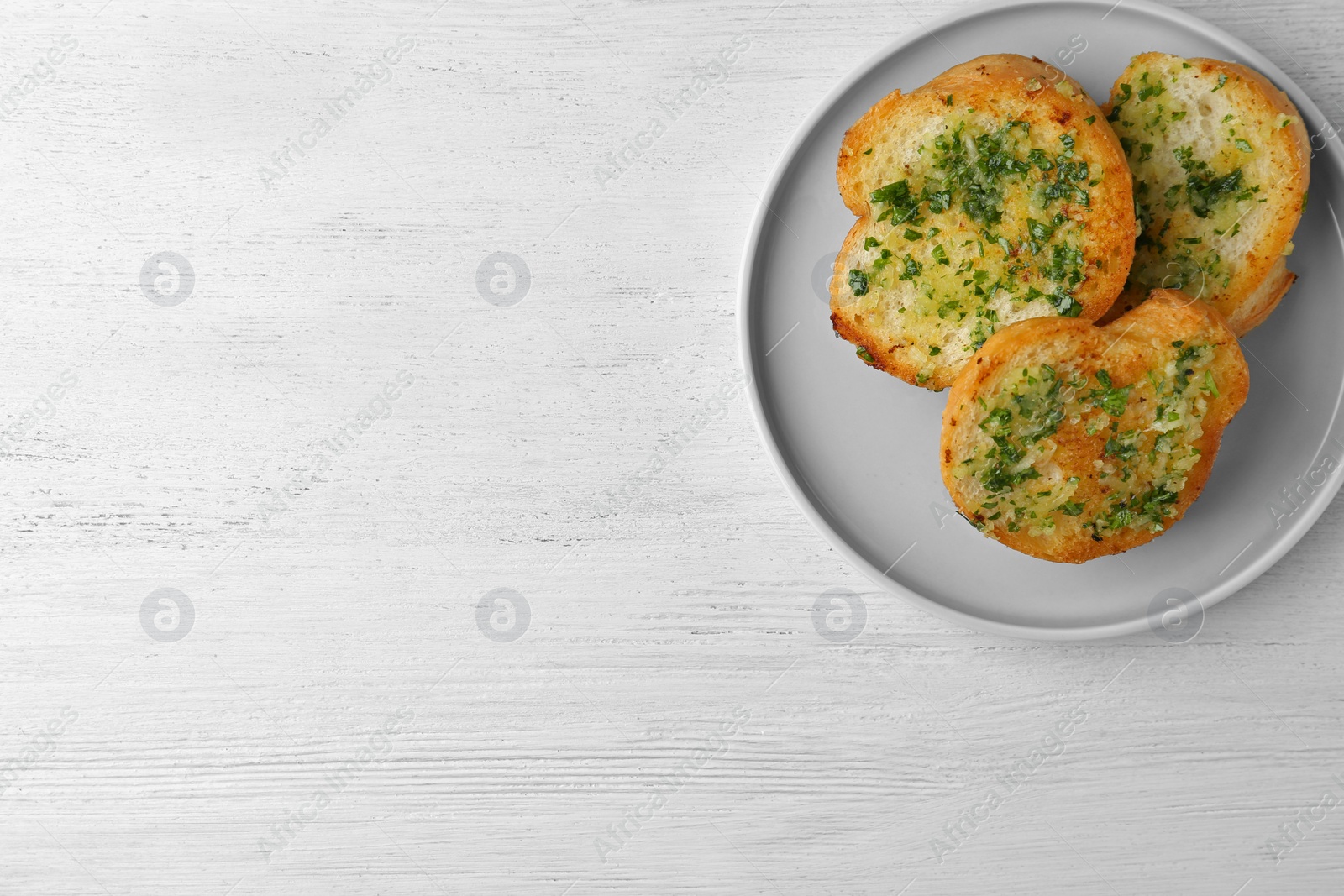 Photo of Slices of toasted bread with garlic and herbs on white wooden table, top view. Space for text