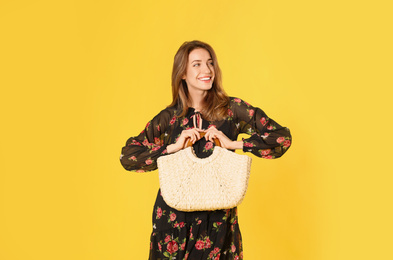 Photo of Young woman wearing floral print dress with straw bag on yellow background