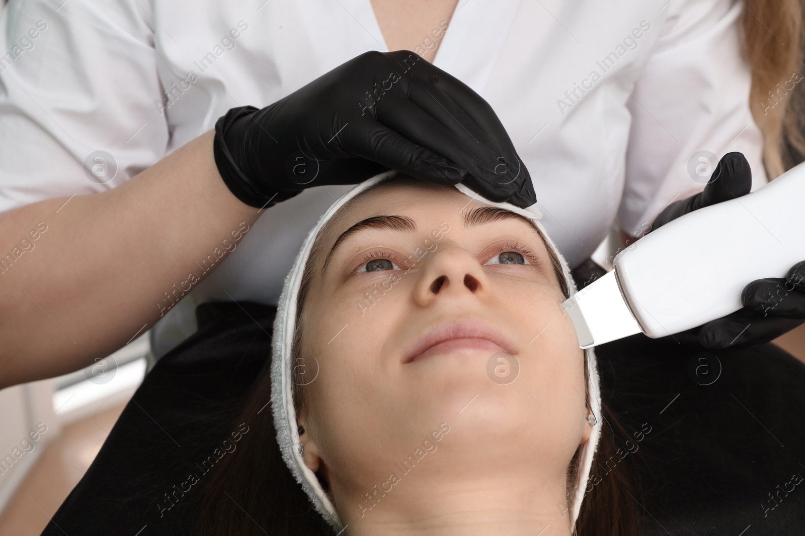 Photo of Cosmetologist using ultrasonic scrubber, closeup. Client having cleansing procedure indoors