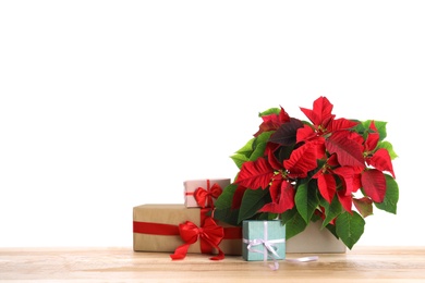 Photo of Red Poinsettia in pot and gifts on wooden table, space for text. Christmas traditional flower