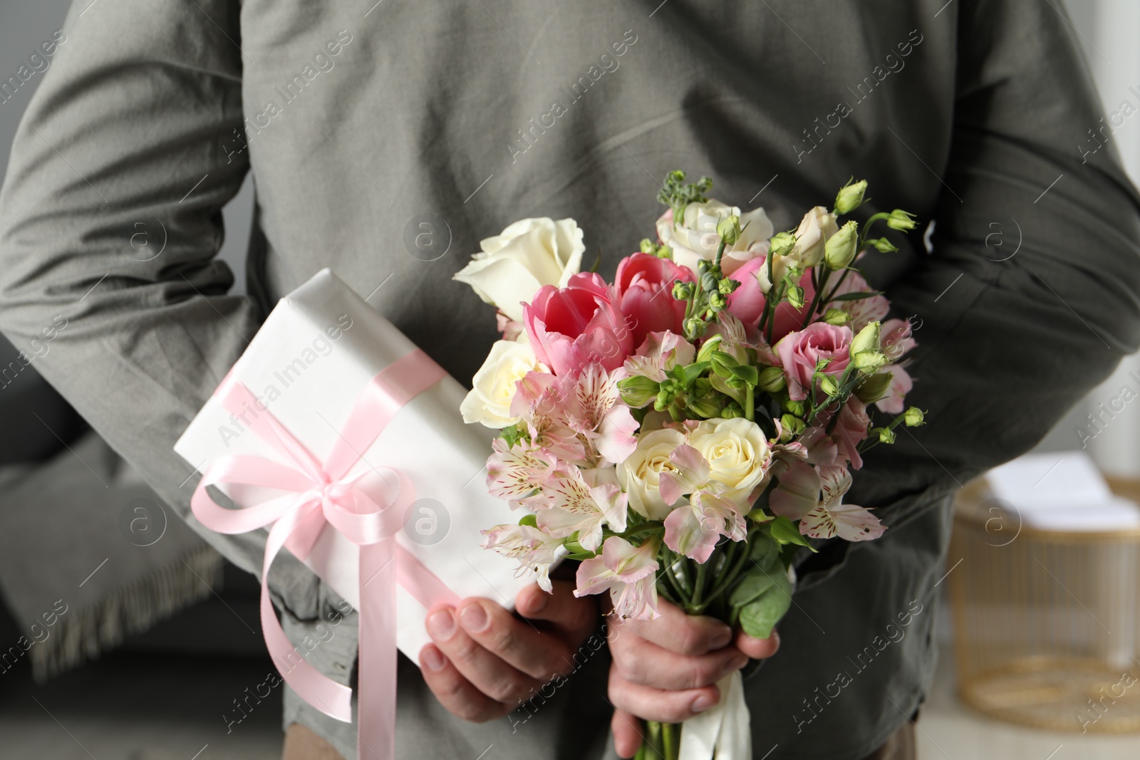 Photo of Man hiding bouquet of flowers and present indoors, closeup