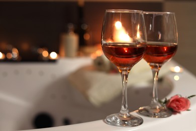 Photo of Wine in glasses and rose on edge of bath indoors. Romantic atmosphere