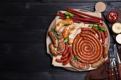 Photo of Different delicious sausages and sauces on black wooden table, flat lay with space for text. Assortment of beer snacks