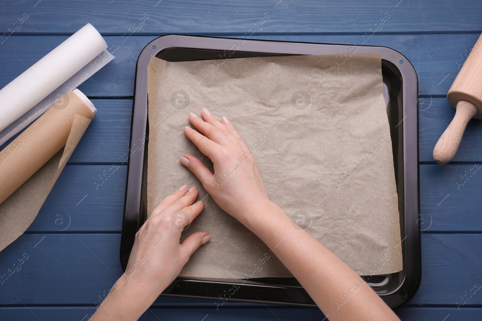 Photo of Woman putting parchment paper in baking pan at blue wooden table, top view