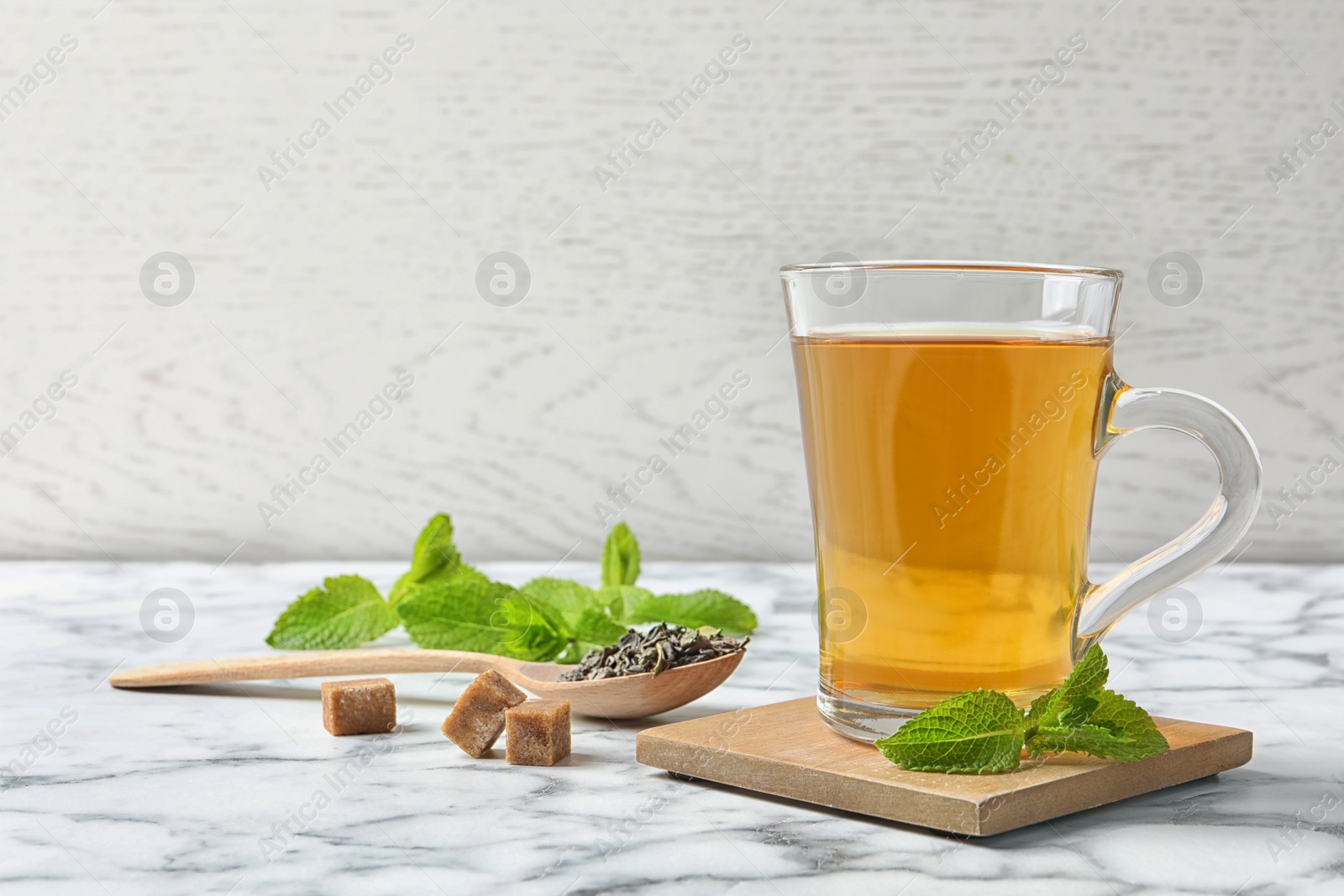 Photo of Cup of hot aromatic mint tea and spoon with dry leaves on marble table