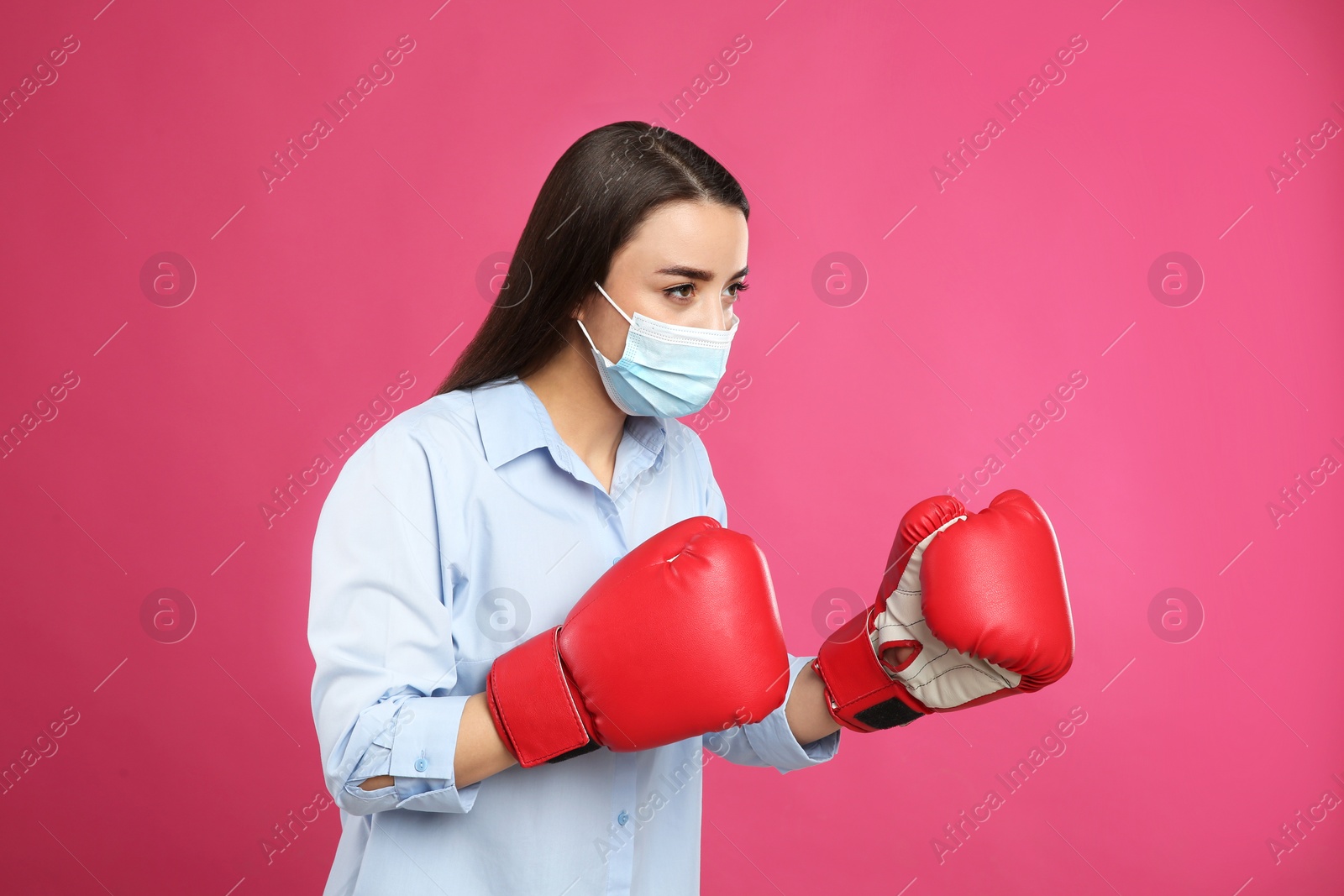 Photo of Woman with protective mask and boxing gloves on pink background. Strong immunity concept