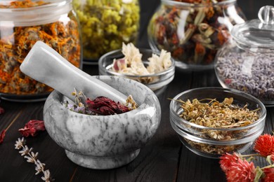 Mortar with pestle and many different herbs on wooden table, closeup