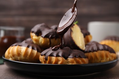 Photo of Pouring chocolate cream onto delicious profiterole on table, closeup