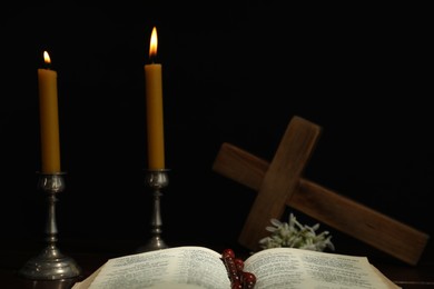 Photo of Church candles, Bible, cross and rosary beads on table against black background