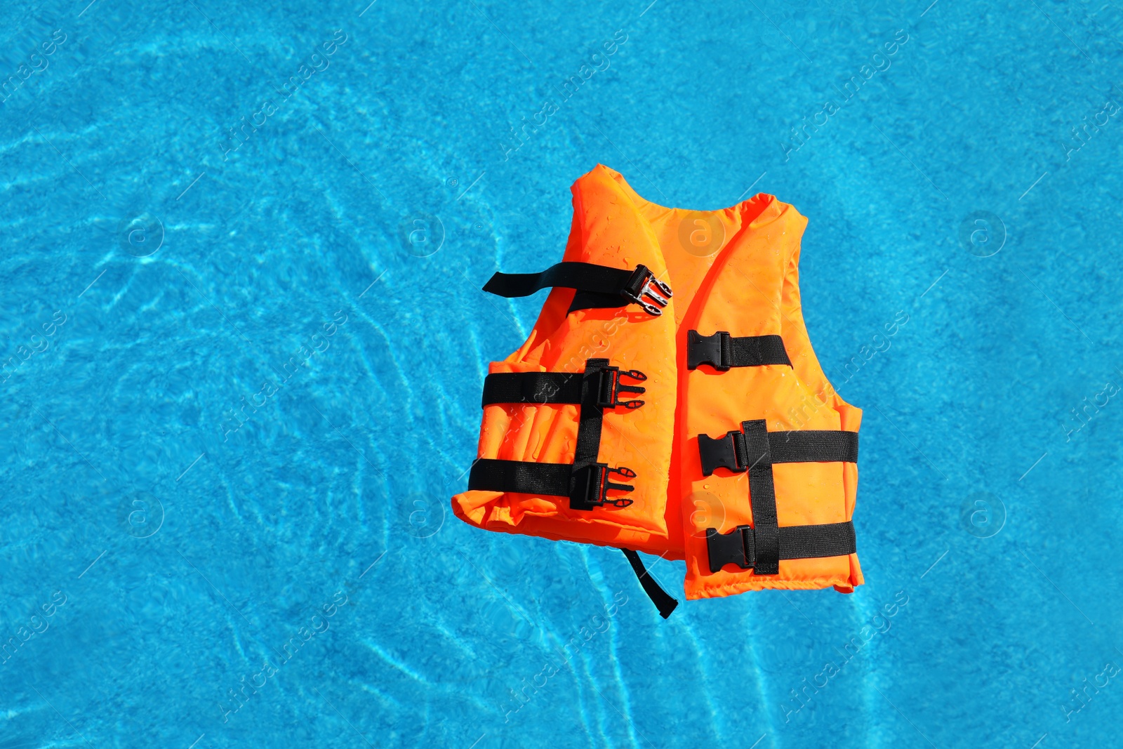 Photo of Bright orange life jacket floating in swimming pool, top view