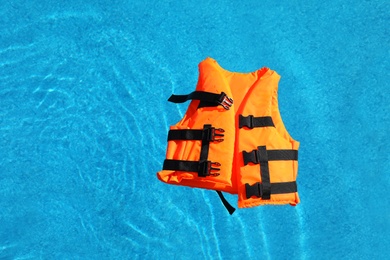 Photo of Bright orange life jacket floating in swimming pool, top view