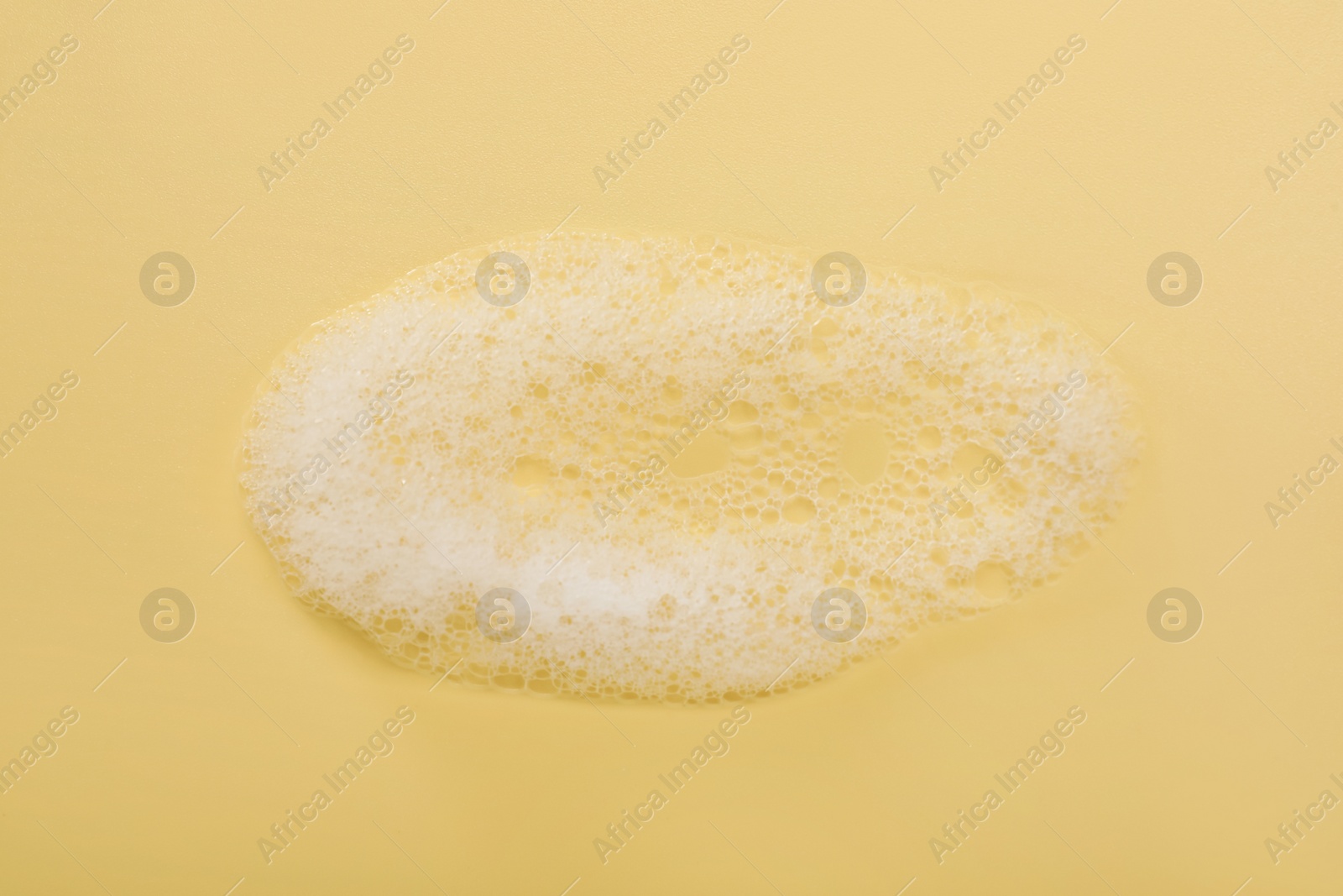 Photo of Spot of white washing foam on yellow background, top view