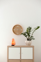 Photo of Himalayan salt lamp and plant on cabinet against white wall