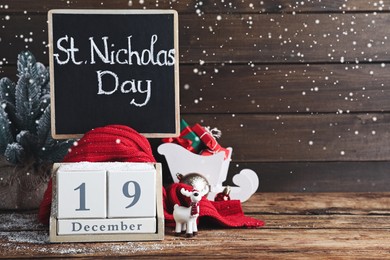 Photo of Saint Nicholas Day. Block calendar with date December 19, small chalkboard and festive decor on wooden table, space for text