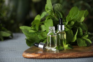 Photo of Bottles of mint essential oil, pipette and green leaves on grey wooden table, space for text