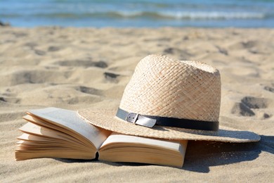 Photo of Open book and straw hat on sandy beach near sea