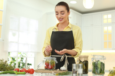 Woman putting garlic into pickling jar at table in kitchen