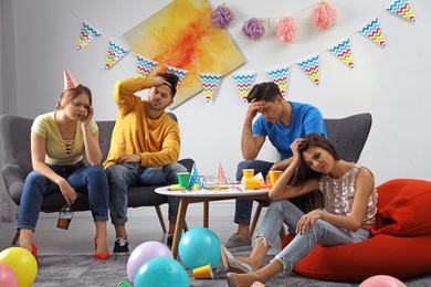 Photo of Group of friends suffering from hangover in messy room after party