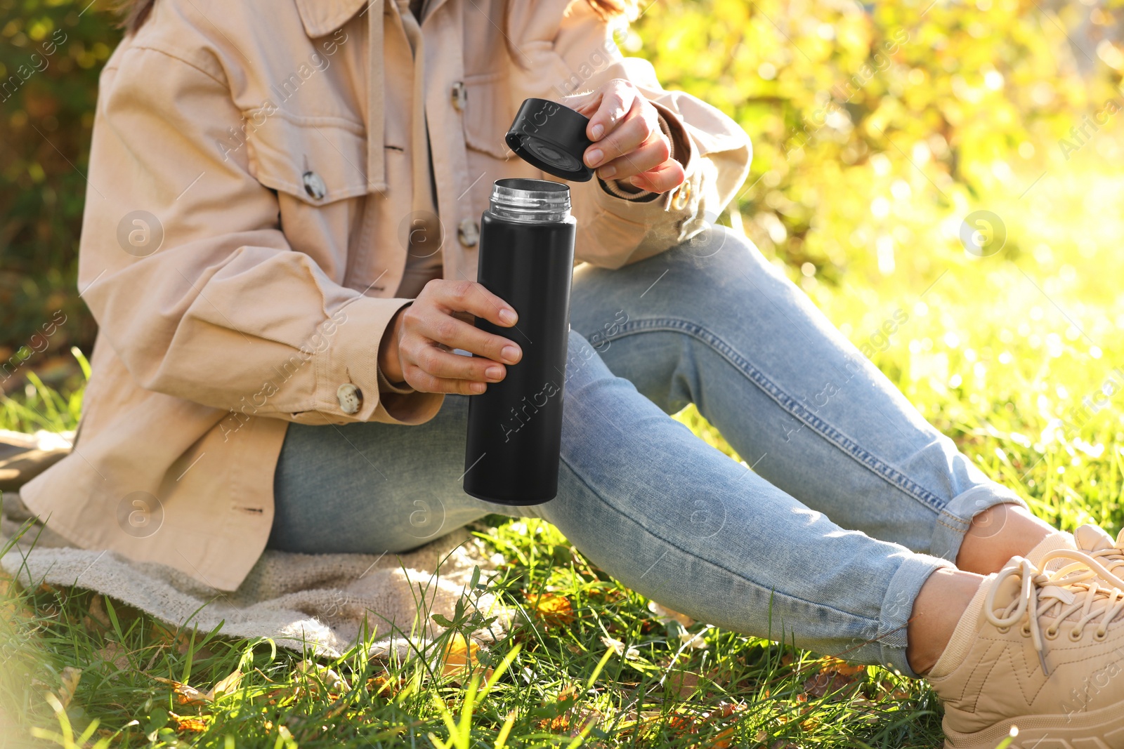 Photo of Woman opening thermos on green grass outdoors, closeup