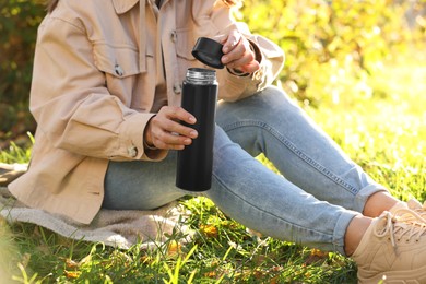 Photo of Woman opening thermos on green grass outdoors, closeup