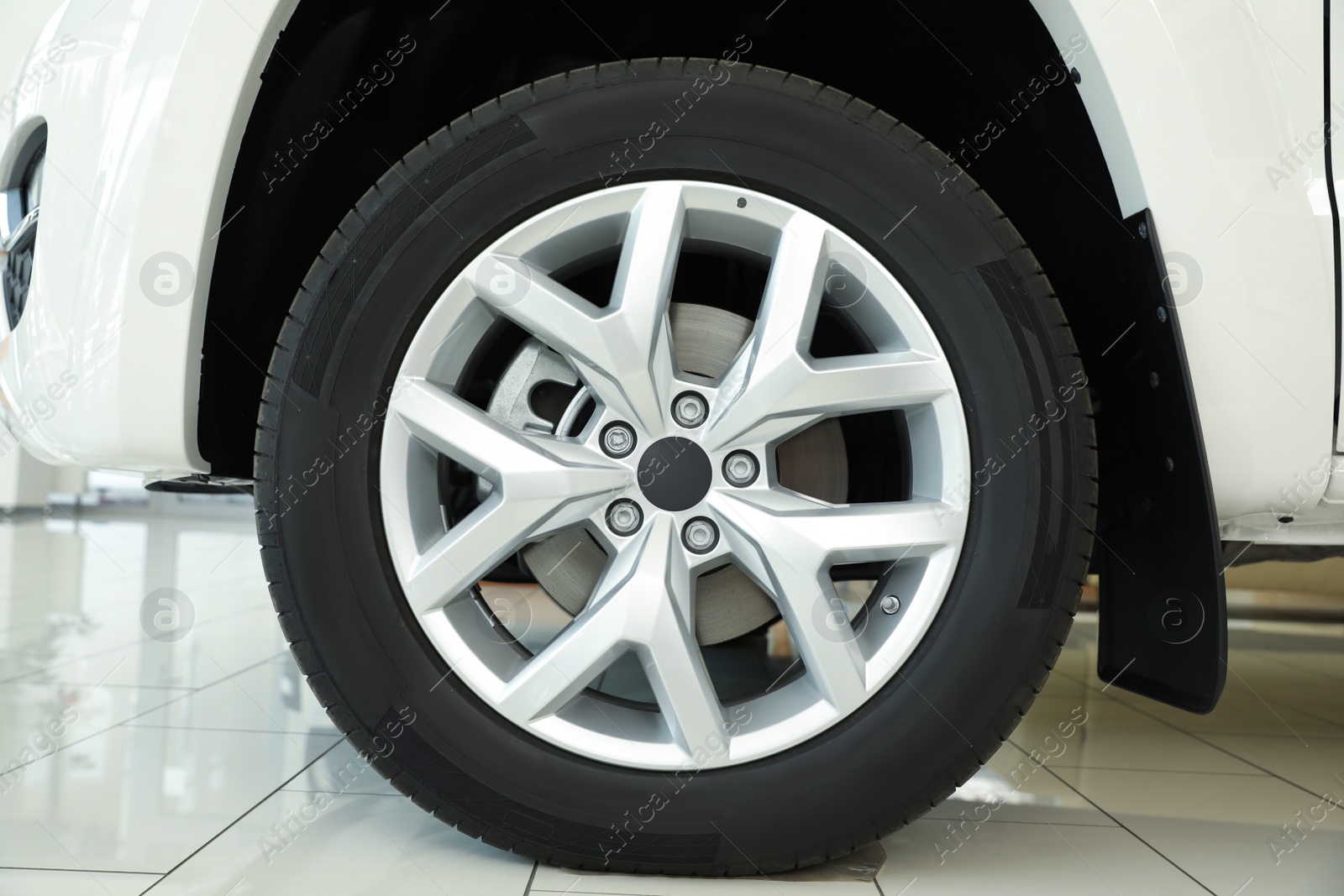 Photo of Wheel of new luxury white car in modern auto dealership, closeup