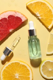 Bottle of cosmetic serum and sliced citrus fruits on yellow background, flat lay