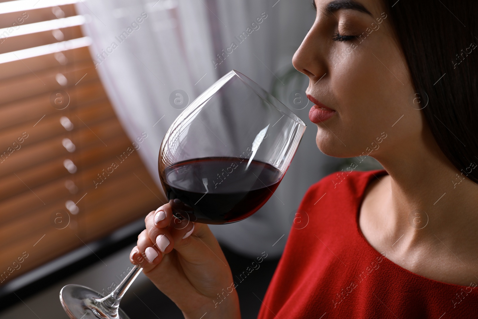 Photo of Beautiful young woman with glass of luxury red wine indoors, closeup view. Space for text