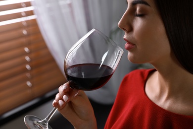 Photo of Beautiful young woman with glass of luxury red wine indoors, closeup view. Space for text