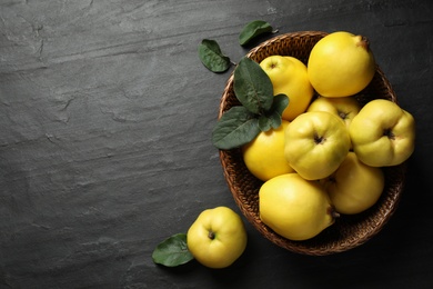 Photo of Fresh ripe organic quinces with leaves on black table, flat lay. Space for text